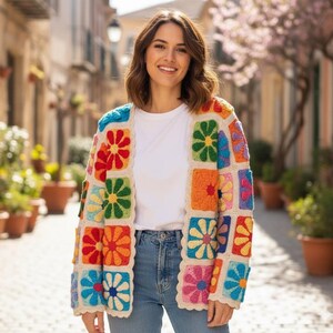 Könnte beinhalten: Bunter Häkelcardigan mit quadratischen Blumenmustern in Rot, Orange, Gelb, Grün, Blau und Pink. Der Cardigan hat einen cremefarbenen Rand und wird über einem weißen T-Shirt und einer blauen Jeans getragen.