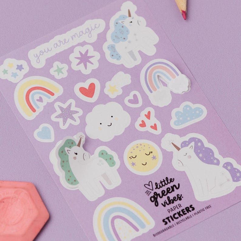 Rainbows & Unicorns party bag filler sticker sheet featuring whimsical pastel illustrations of magical unicorns, colourful rainbows, floating hearts, smiling clouds, stars, and gift boxes on a lilac background, accompanied by pencils for colouring, plastic-free