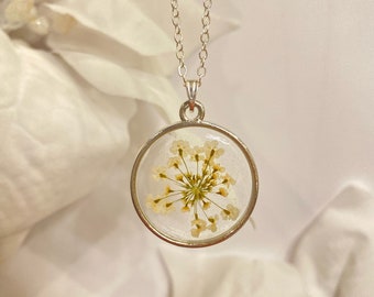 Könnte beinhalten: Eine silberne Kettenkette mit einem runden Anhänger, der eine gepresste weiße Blume mit grünem Zentrum zeigt.
