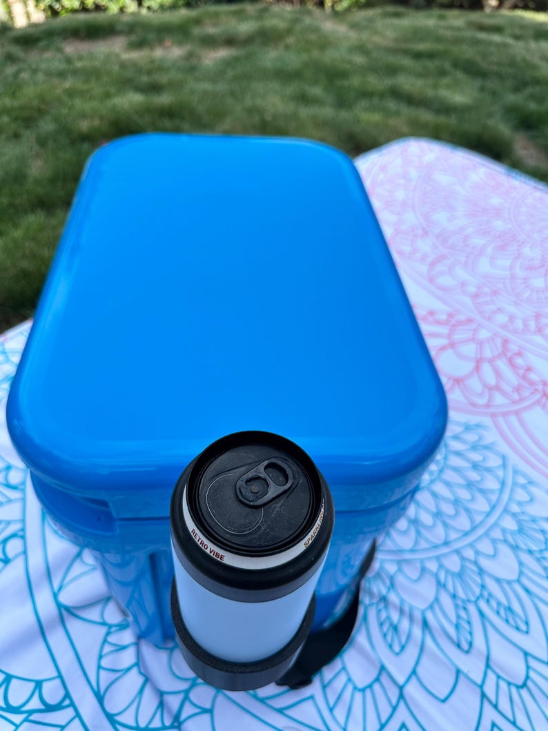 Op de afbeelding: Een blauwe koelbox met een zwart-witte blikjeskoeler. Op de blikjeskoeler staat de tekst "Retro Vibe". De koelbox en de blikjeskoeler liggen op een patroon deken.