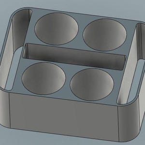 May include: A gray, rectangular organizer with four circular compartments and a central divider. The organizer has rounded edges and a handle-like opening on each side, suggesting a design for holding small items or containers.