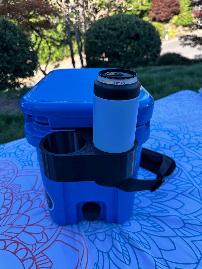 Op de afbeelding: Een blauwe koeler met een zwarte bekerhouder en een lichtblauwe blikjeskoeler. Op de blikjeskoeler staat "Retro Vibe". De koeler heeft een zwarte riem en staat op een patroon deken.