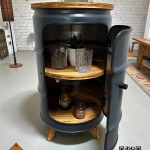 Könnte beinhalten: Ein dunkelgrauer, fassförmiger Schrank mit einer Holzplatte und Regalen. Die Schranktür ist geöffnet und zeigt zwei Regale mit dekorativen Gegenständen. Der Schrank wird von Holzbeinen getragen und hat einen Griff. Der Schrank hat ein "LOFT DESIGN"-Logo.