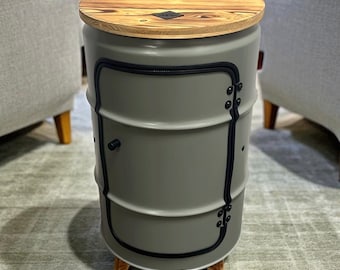 May include: A gray metal barrel side table with a wooden top. The table has a door and is accented with black trim and hardware. The base is made of wood. The text "LOFT DESIGN" is visible on a diamond-shaped orange sign.