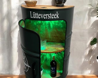 May include: A dark green barrel-shaped cabinet with a wooden top and interior shelves. The cabinet door is open, revealing a green illuminated interior with a bottle of wine and a glass. The text "Lütteversteek" is displayed on the front.