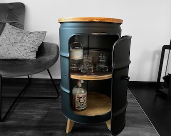 May include: A matte black metal barrel cabinet featuring a circular wooden top and two internal wooden shelves. The cabinet has a hinged door with a small handle, revealing glass bottles and two clear drinking glasses stored inside.