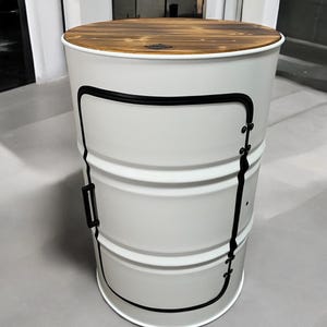 Peut inclure: Une table d'appoint en forme de baril en métal blanc avec un dessus rond en bois. Le baril a des garnitures noires et une poignée noire. Le dessus est fait de planches de bois. La table est adaptée à l'intérieur.