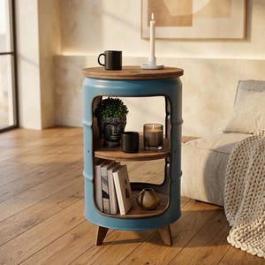 Peut inclure: Une table d'appoint cylindrique en métal bleu avec un plateau circulaire en bois et deux étagères intérieures en bois. La table présente une découpe, trois pieds en bois et supporte une tasse noire, une bougie, un pot Bouddha et des livres.