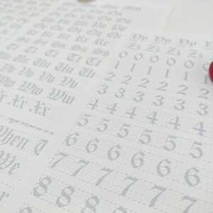 May include: A white sheet of paper with a grid pattern and numbers 0 through 9 written in a cursive font. The numbers are repeated multiple times in rows. The paper is partially covered by two red yo-yos.
