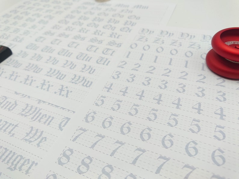 May include: A white sheet of paper with a grid pattern and numbers 0 through 9 written in a cursive font. The numbers are repeated multiple times in rows. The paper is partially covered by two red yo-yos.