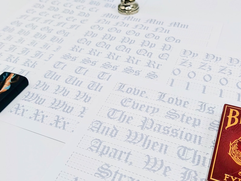 May include: A white sheet of paper with a grid pattern and gray lettering. The letters are in a gothic font and include the alphabet, numbers, and the phrase "Love is Every Step".