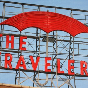 May include: A red umbrella hangs over a metal sign that reads "THE TRAVELERS". The sign is against a blue sky.