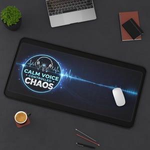 May include: Black rectangular desk mat with the text "CALM VOICE CONTROLLED CHAOS" in a blue and white design. The mat features a graphic of headphones and a sound wave. A white mouse is on the right side of the mat.