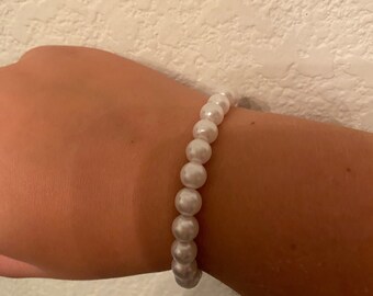 Peut inclure: Un bracelet en perles blanches avec un design simple. Le bracelet est composé de petites perles rondes enfilées sur un cordon élastique transparent.