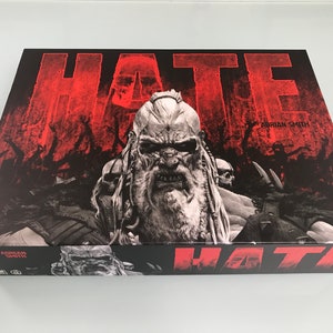 May include: A board game box with a black background and red text that reads "HATE". The box features a menacing-looking man with a long beard and a skull on his shoulder. The text "Adrian Smith" is visible in the upper right corner of the box.