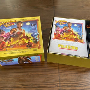 Puede incluir: Una caja amarilla con un tablero de juego en su interior. La caja tiene una imagen de Kurt Russell en la parte delantera. El juego se llama "Big Trouble in Little China: The Game".