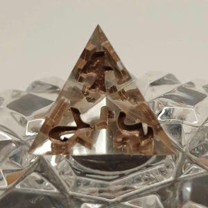 May include: A clear pyramid-shaped object with brown internal structures. The pyramid is set on a clear, faceted surface. The brown elements appear to be decorative and add a unique aesthetic to the piece.