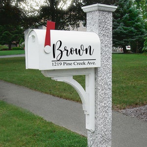 May include: White mailbox with the name "Brown" in a cursive font and the address "1219 Pine Creek Ave." in a simple font. The mailbox has a red flag and is mounted on a white bracket attached to a stone pillar.