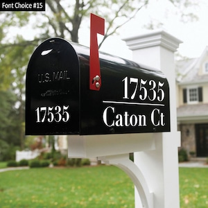 A black mailbox sitting on a nice white mailbox pole. The mailbox has a nice white address decal that displays “17535 Caton CT” The number is separated from the street address by a horizontal line. There is a  small 17535 number on the front lid.