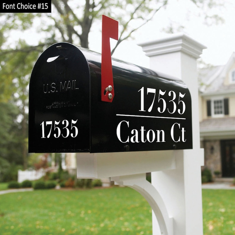 A black mailbox sitting on a nice white mailbox pole. The mailbox has a nice white address decal that displays “17535 Caton CT” The number is separated from the street address by a horizontal line. There is a  small 17535 number on the front lid.