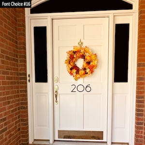May include: A white front door with a fall-themed wreath and the number 206 on it. The door is surrounded by brick.