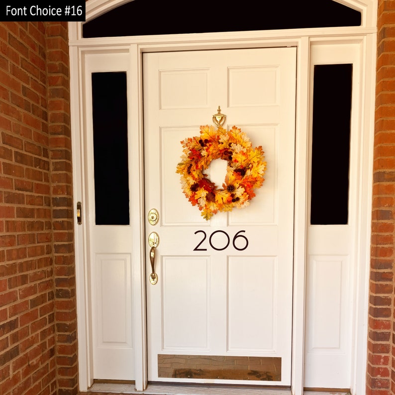 May include: A white front door with a fall-themed wreath and the number 206 on it. The door is surrounded by brick.