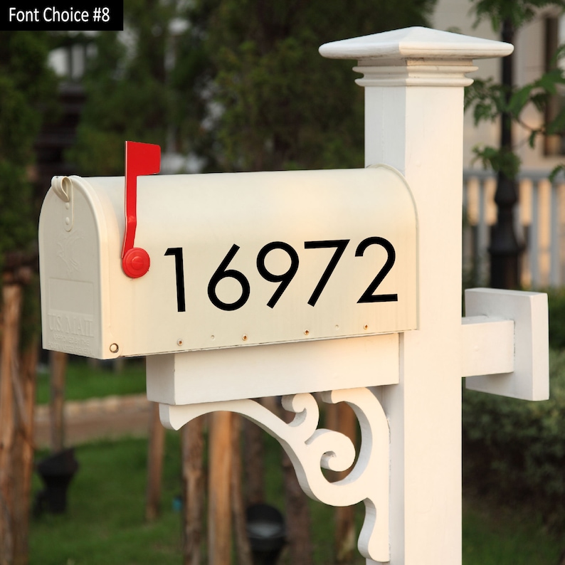 May include: White mailbox with a red flag and black numbers "16972" on the front. The mailbox is mounted on a white post.