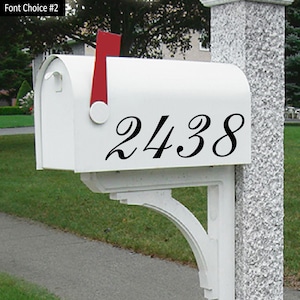 May include: White mailbox with a black cursive number 2438 on the front. The mailbox is mounted on a white post.