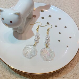Könnte beinhalten: Ein Paar Ohrringe aus irisierendem, weißem Muschelschmuck mit goldenen Haken und Perlenakzenten.