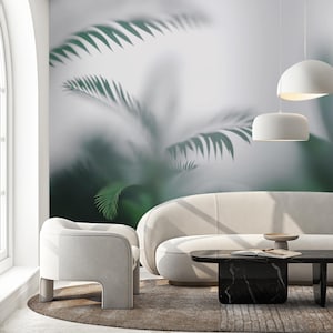 May include: A modern living room with a neutral color palette. A white sofa and armchair sit on a round rug. A black marble coffee table and two white pendant lights are also present. A large mural of green palm leaves adorns the wall.