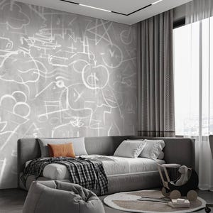 Op de afbeelding: Een moderne slaapkamer met een grijze slaapbank, kussens en een geruite deken. De grijze muur is versierd met witte abstracte tekeningen. Een kleine houten speelgoedkinderwagen en een rond tapijt met geometrische vormen zijn ook aanwezig.
