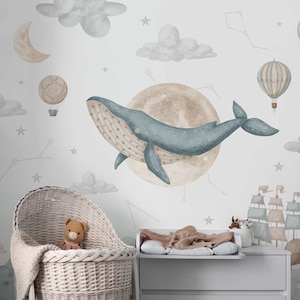 May include: A whimsical nursery wall mural featuring a blue whale, hot air balloons, clouds, stars, and a crescent moon. The design includes a wicker bassinet with a teddy bear and a changing table.