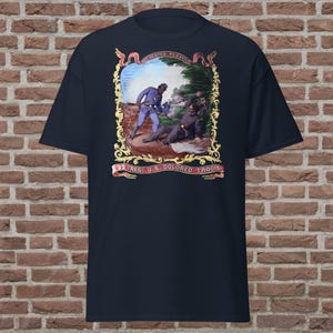 May include: A navy blue t-shirt featuring a gold framed image of two soldiers in a battle scene. The image is surrounded by text that reads "We Conquered" and "22nd Regt. U.S. Colored Troops".