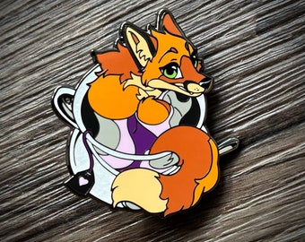 May include: A colorful enamel pin featuring a cartoon fox wearing a purple and pink swimsuit, with its tail wrapped around its body. The fox is inside a white and gray space helmet with a heart-shaped tag.