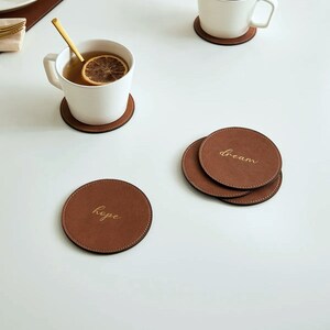 May include: Four brown leather coasters with gold lettering. The coasters feature the words "hope" and "dream".