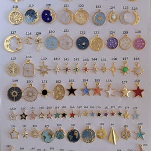 Puede incluir: Una colecci&oacute;n de colgantes dorados con diversos dise&ntilde;os celestiales y de viaje. Los colgantes incluyen soles, lunas, estrellas, planetas y otros elementos decorativos. Los colgantes est&aacute;n dispuestos sobre una superficie blanca.