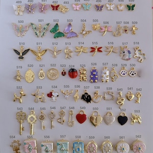 Puede incluir: Una colecci&oacute;n de colgantes dorados en varias formas, incluyendo mariposas, llaves, corazones y animales. Los colgantes est&aacute;n dispuestos sobre una superficie blanca, cada uno etiquetado con un n&uacute;mero. Adecuado para la creaci&oacute;n de joyas.