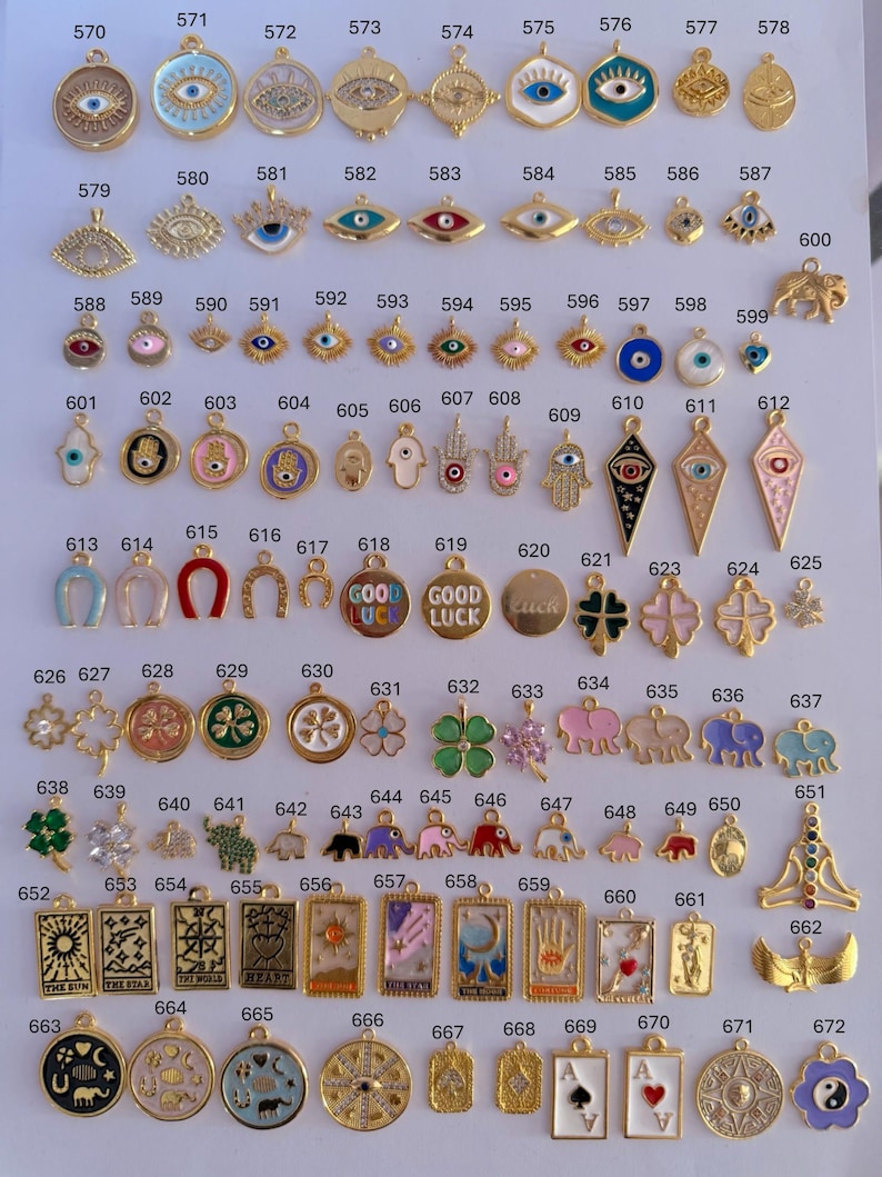 Puede incluir: Una colecci&oacute;n de colgantes y dijes dorados, con varios dise&ntilde;os como ojos turcos, manos de F&aacute;tima, tr&eacute;boles de cuatro hojas, elefantes y motivos de cartas del tarot. Los dijes est&aacute;n dispuestos sobre una superficie blanca.