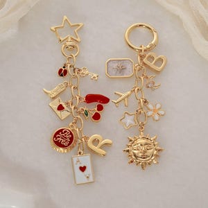 May include: Two gold-colored charm keychains with various charms, including a star, ladybug, cherries, and a playing card. One keychain has the text "Be Free" on a charm. The other has a sun charm.
