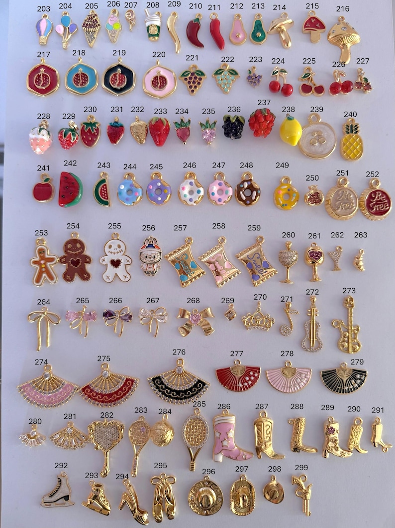 Puede incluir: Una colecci&oacute;n de abalorios dorados con diversos dise&ntilde;os, incluyendo frutas, postres, instrumentos musicales y lazos. Los abalorios est&aacute;n dispuestos sobre una superficie blanca, mostrando sus intrincados detalles y variados temas.