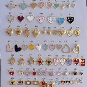Puede incluir: Una colecci&oacute;n de colgantes y abalorios en forma de coraz&oacute;n en varios colores y dise&ntilde;os. Los colgantes incluyen acabados dorados, plateados y esmaltados, algunos con texto y adornos. La imagen muestra una variedad de estilos.