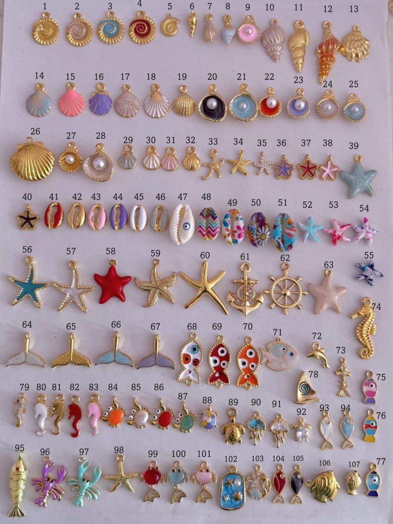 Puede incluir: Una colecci&oacute;n de abalorios dorados y coloridos en varias formas, incluyendo conchas marinas, estrellas de mar y criaturas marinas. Estos abalorios son adecuados para la fabricaci&oacute;n de joyas y proyectos de artesan&iacute;a. Los abalorios est&aacute;n dispuestos sobre una superficie blanca.