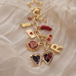 Puede incluir: Una pulsera de dijes dorada con varios dijes, incluyendo una estrella, una llave, un chile, un relicario en forma de coraz&oacute;n con una foto y un dije que dice "Be Free". Los dijes est&aacute;n suspendidos de una delicada cadena.