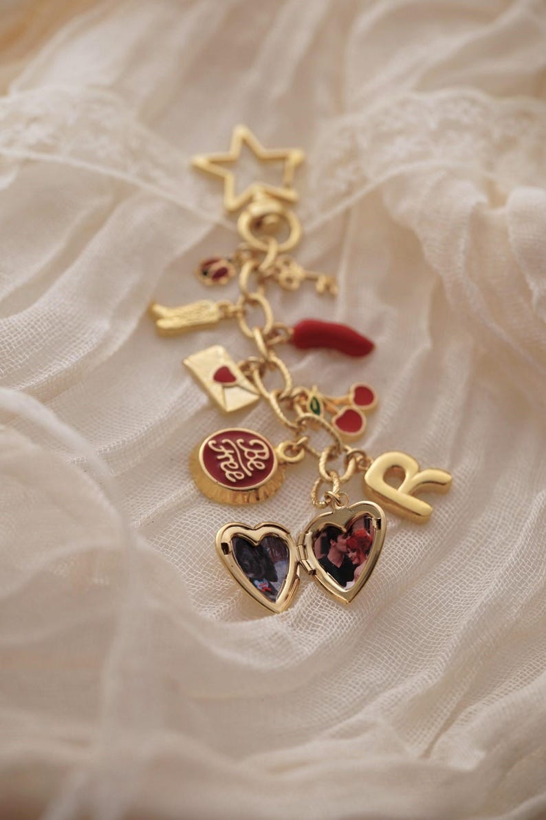 Puede incluir: Una pulsera de dijes dorada con varios dijes, incluyendo una estrella, una llave, un chile, un relicario en forma de coraz&oacute;n con una foto y un dije que dice "Be Free". Los dijes est&aacute;n suspendidos de una delicada cadena.