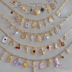 May include: A gold chain necklace with various charms, including a heart, cross, star, horseshoe, cherry, gun, butterfly, and a boot. The charms are attached to the chain with jump rings. The chain is on a white background.