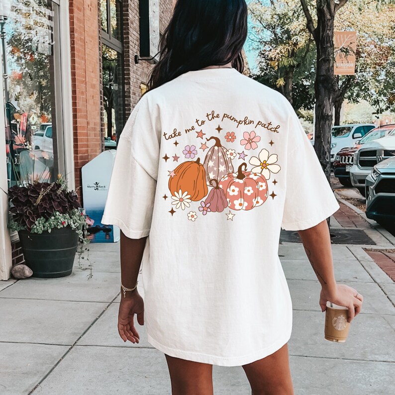 May include: White t-shirt with a graphic of pumpkins and flowers. The text "take me to the pumpkin patch" is printed on the shirt.