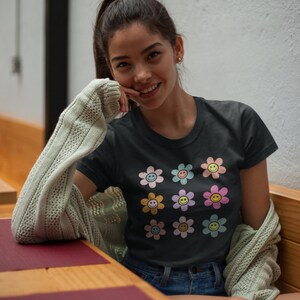 May include: A black t-shirt featuring a colourful pattern of smiley face flowers. The flowers are in shades of pink, blue, yellow, and green.