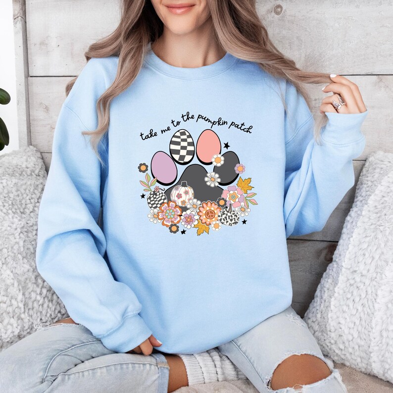 May include: Light blue sweatshirt with a paw print design featuring a checkered pattern, pumpkins, and flowers. The text "Take me to the pumpkin patch" is written above the paw print.