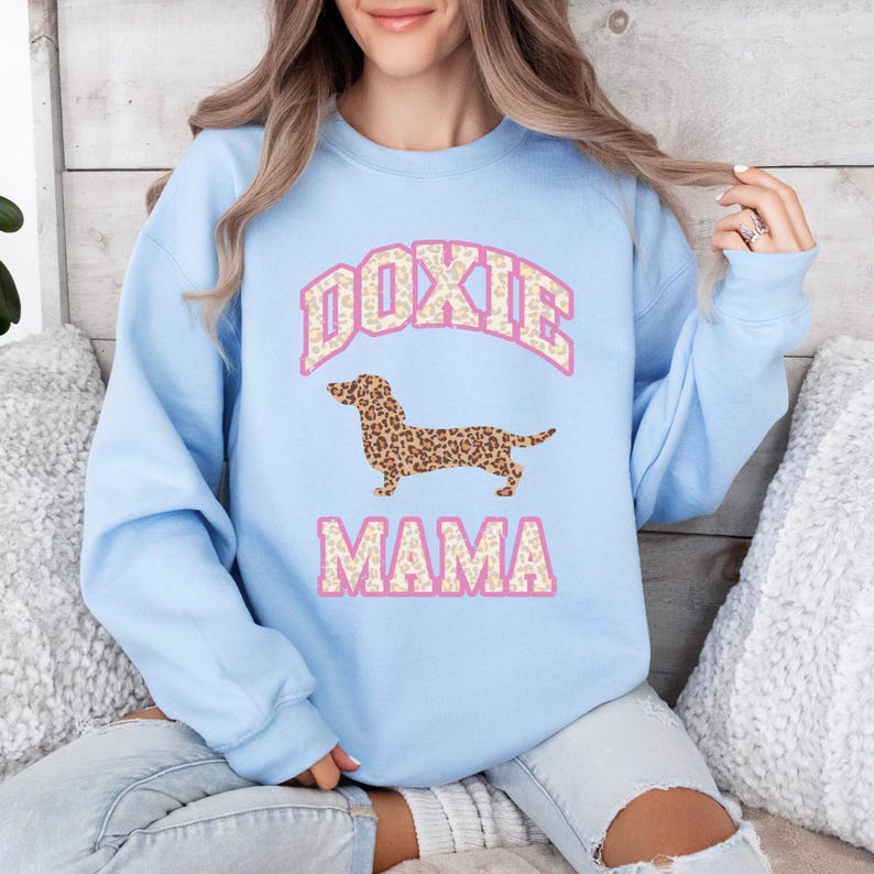 May include: Light blue sweatshirt with a pink "Doxie Mama" graphic featuring a dachshund with a leopard print pattern.