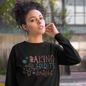 May include: Black sweatshirt with a festive design featuring a gingerbread man, snowflakes, and the text "Baking Spirits Bright".